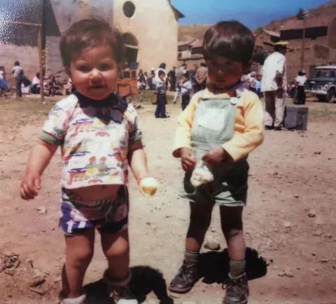 Two small children stand in a dusty street, in an old colour photograph.